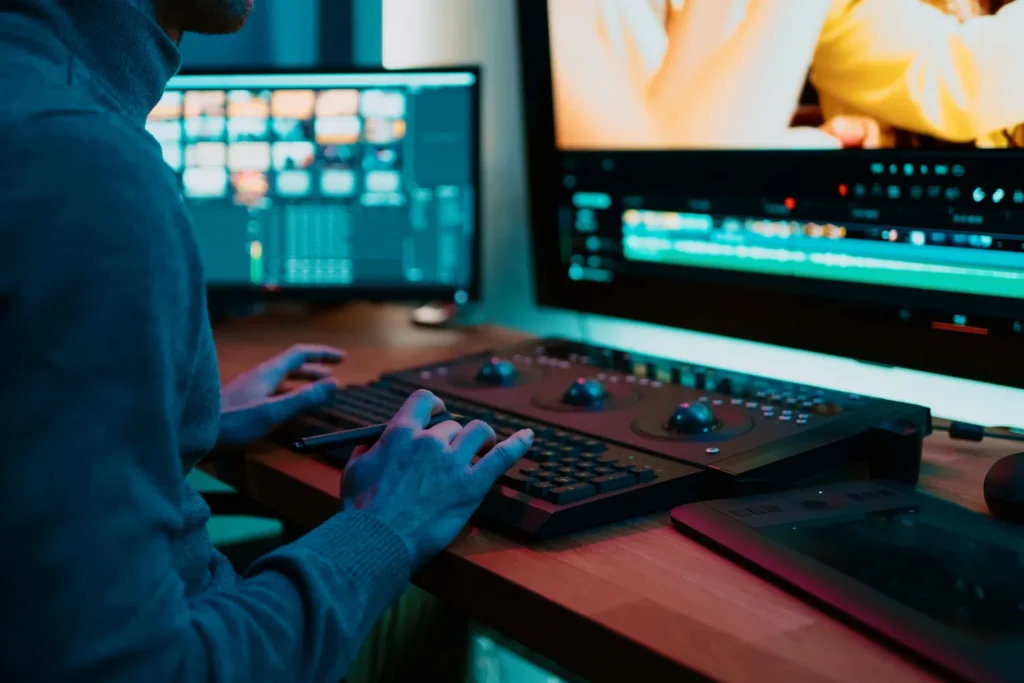 Video editor working at dual monitors with a color grading control panel.